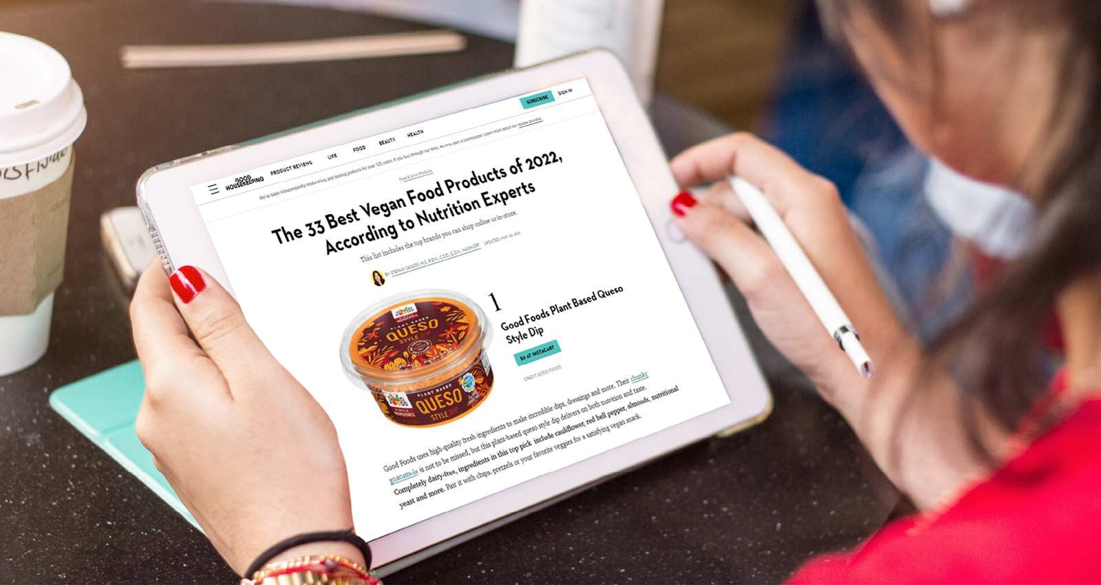 Women looking at an iPad that has a Good Housekeeping article on it featuring Good Foods Plant Based Queso Style Dip at number 1 on an article titled "The 33 Best Vegan Food Products of 2022, According to Nutrition Experts"