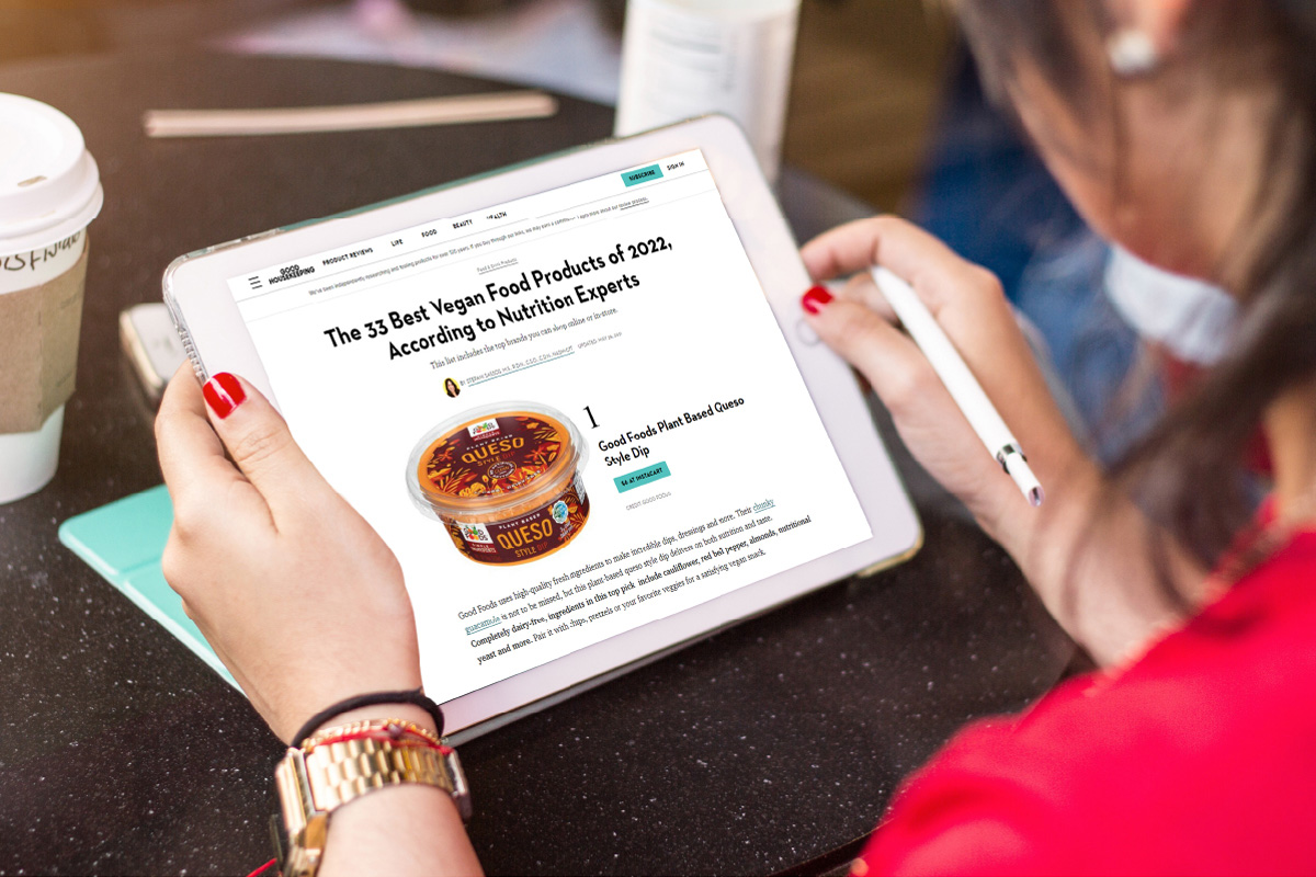 Women looking at an iPad that has a Good Housekeeping article on it featuring Good Foods Plant Based Queso Style Dip at number 1 on an article titled "The 33 Best Vegan Food Products of 2022, According to Nutrition Experts"